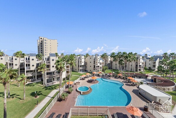A resort with a central swimming pool, multiple balconies, and palm trees.