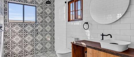 A bathroom with patterned tiles, a wooden vanity, a white sink, and a window.