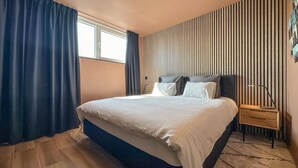 A bedroom with a large bed, a nightstand, a window with curtains, and a striped wall.