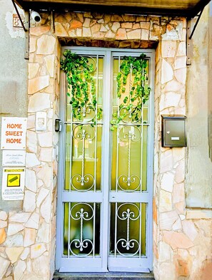 A stone facade with a metal door featuring decorative ironwork and green vines.