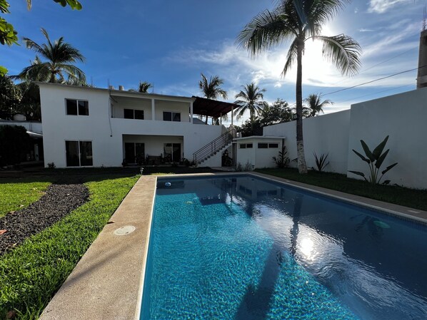 Relax by the rectangular pool surrounded by a lush lawn and palm trees.