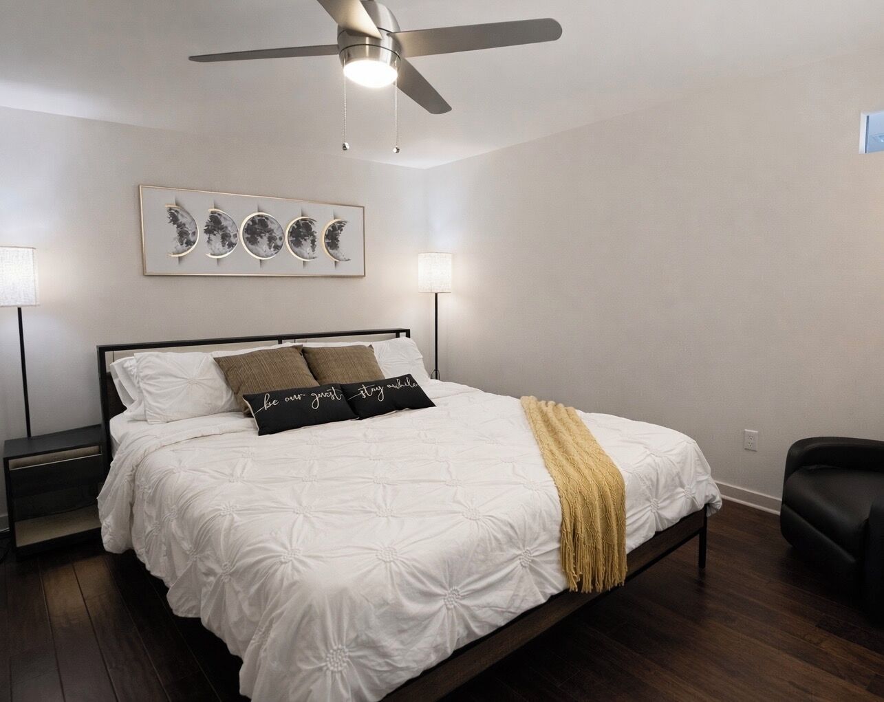 Ein Schlafzimmer mit einem Bett, einem Deckenventilator, einer Wandleuchte und einem gerahmten Kunstwerk über dem Bett.