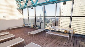 A rooftop terrace with wooden flooring, several lounge chairs, and a view of the cityscape through large windows. - Cozy Retreat with Rooftop Pool, Parking, and Spacious Comfort (Dallas)