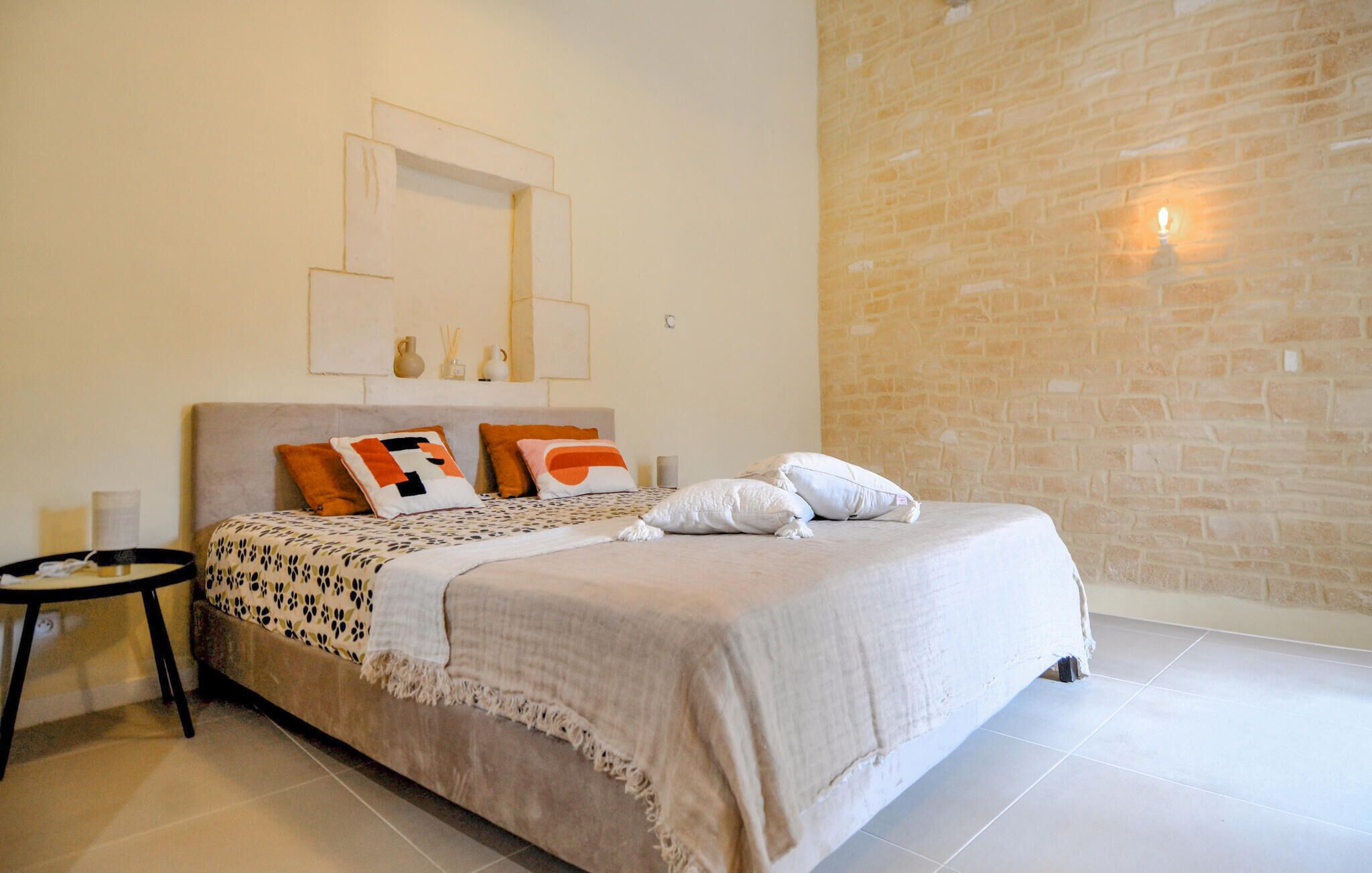 A bedroom with a bed, pillows, a nightstand, and a stone wall.