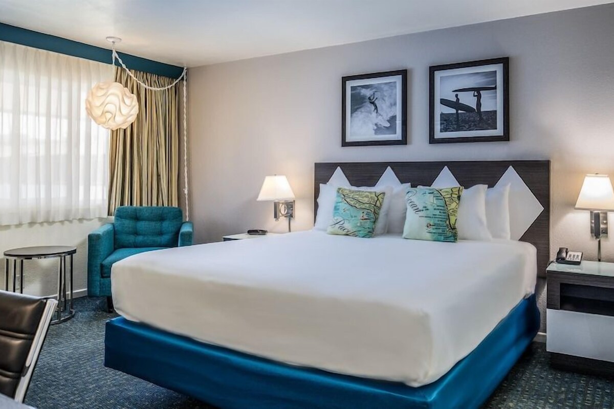 A hotel room with a large bed, two side tables with lamps, a chair, a desk, and a window with curtains.