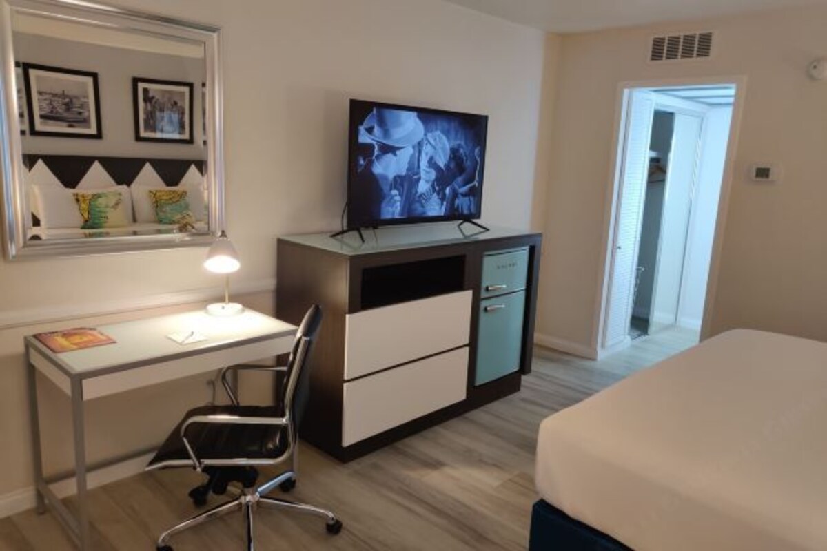 A hotel room with a desk, chair, TV, bed, and a door leading to another room.