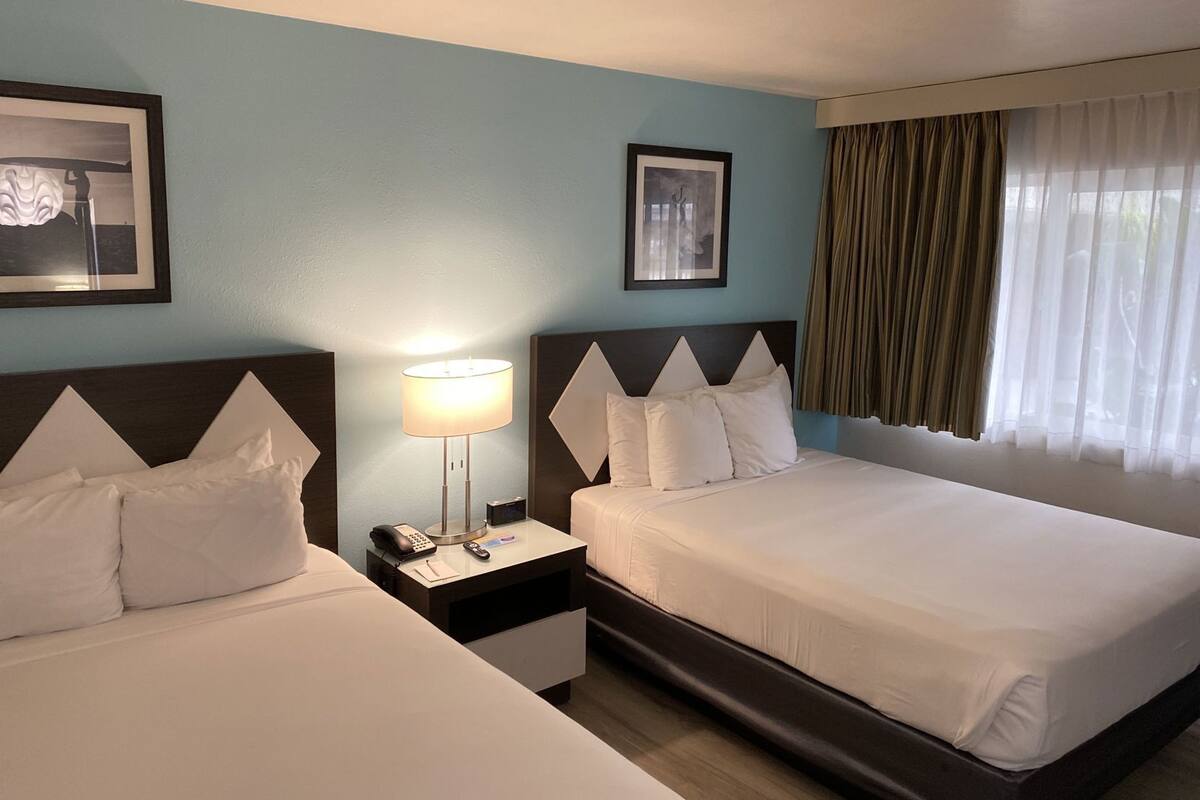 Quarto de hotel com duas camas, uma mesa de cabeceira com abajur, um telefone e um controle remoto.