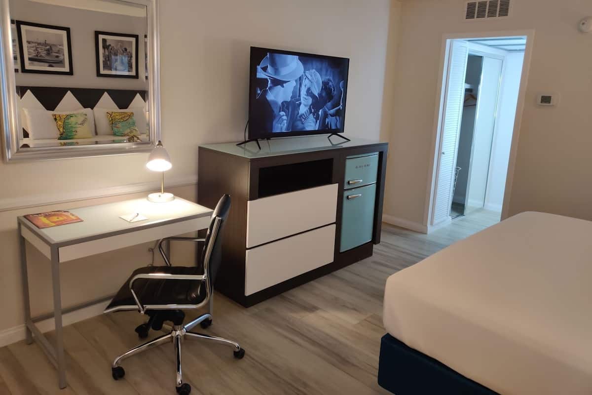 Quarto de hotel com cama, escrivaninha com computador, cadeira, televisão e guarda-roupa.