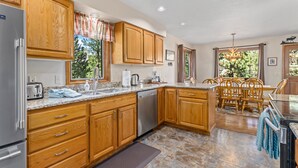 A kitchen with wooden cabinets, granite countertops, a dishwasher, and a dining area with wooden chairs and a table. - Aspen Brook Riversong by Estes Park Homes (Estes Park)