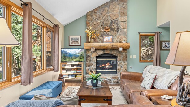 A cozy living room with a stone fireplace, leather sofas, and a bookshelf. - Aspen Brook Riversong by Estes Park Homes (Estes Park)