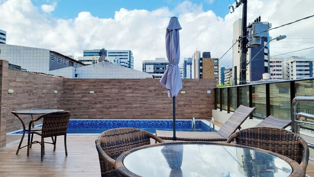 A rooftop terrace with a glass table, wicker chairs, and a pool. - Perto da Praia: Wi-Fi, Piscina e Garagem (Maceió)