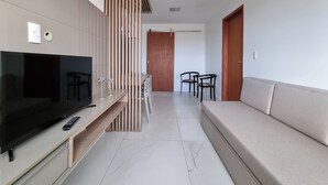 A modern living room with a flat-screen TV, a sofa, a dining table with chairs, and a wooden partition. - Perto da Praia: Wi-Fi, Piscina e Garagem (Maceió)