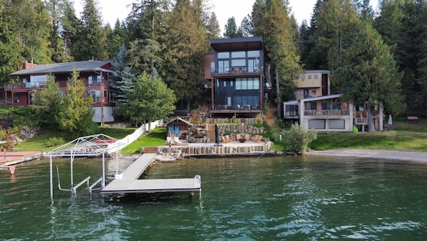 Une propriété au bord du lac comprenant plusieurs bâtiments, notamment une maison moderne dotée de grandes fenêtres et d’une terrasse, ainsi qu’une petite construction de type cabane.