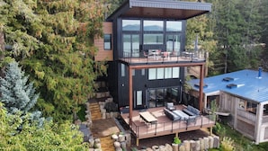 Une cabane moderne à plusieurs niveaux, dotée d’une terrasse, d’un espace salon extérieur et offrant une vue sur la forêt environnante.