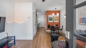 A modern living space with a wooden floor, a dining area with black chairs, and a TV on a black stand. - Htown eclectic funk vibe A (Houston)