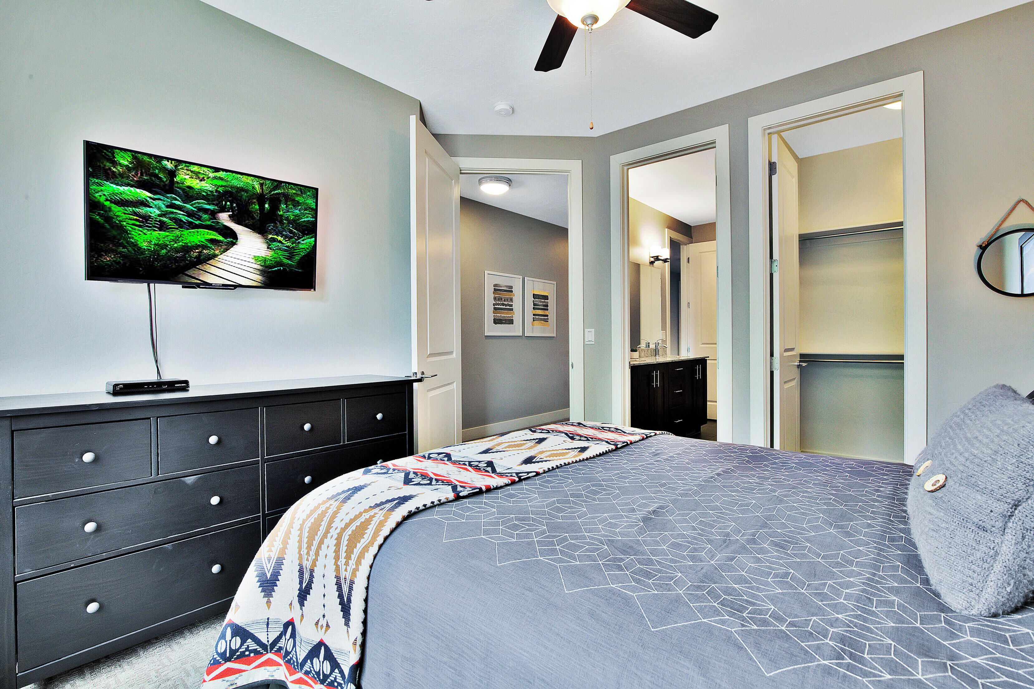 A bedroom with a bed, a dresser, a television on the wall, and a closet.
