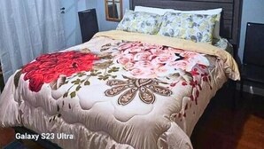 Ein Schlafzimmer mit Galaxy S23 Ultra Bett, einem Fenster mit Vorhängen, einem Holz-Kopfteil und einem an der Wand hängenden Kunstwerk.