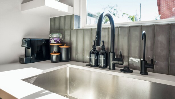 A modern kitchen with a stainless steel sink, black faucets, and a coffee machine.