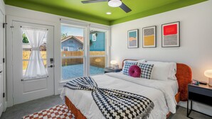 A bedroom with a bed, a ceiling fan, a window with a view of a backyard, and a door with a curtain.