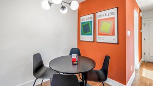 A conference room with a round table, four black chairs, and two framed artworks on the wall.