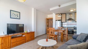 A modern living room with a TV, wooden furniture, a dining table, and a kitchen area.
