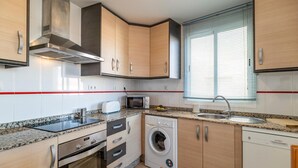 A modern kitchen with stainless steel appliances, a built-in oven, microwave, and washing machine, along with a sink and window with blinds.