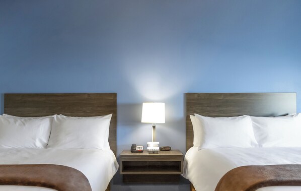 A hotel room with two beds, a nightstand with a lamp, and a phone.