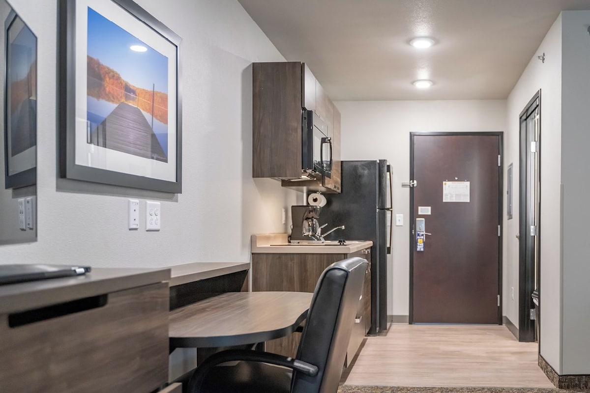 A modern kitchen with wooden cabinets, a built-in oven, and a refrigerator. There is a dining area with a table and chairs.