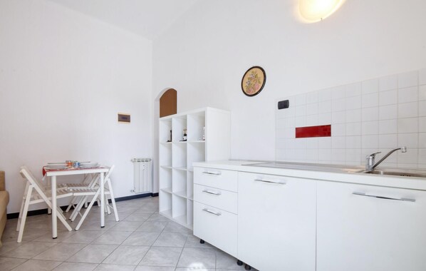 Una cocina compacta con muebles blancos, horno integrado, lavamanos y zona de comedor con una silla y una mesa.
