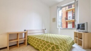 Habitació petita i lluminosa amb un llit, televisió i finestra que dona a un balcó.