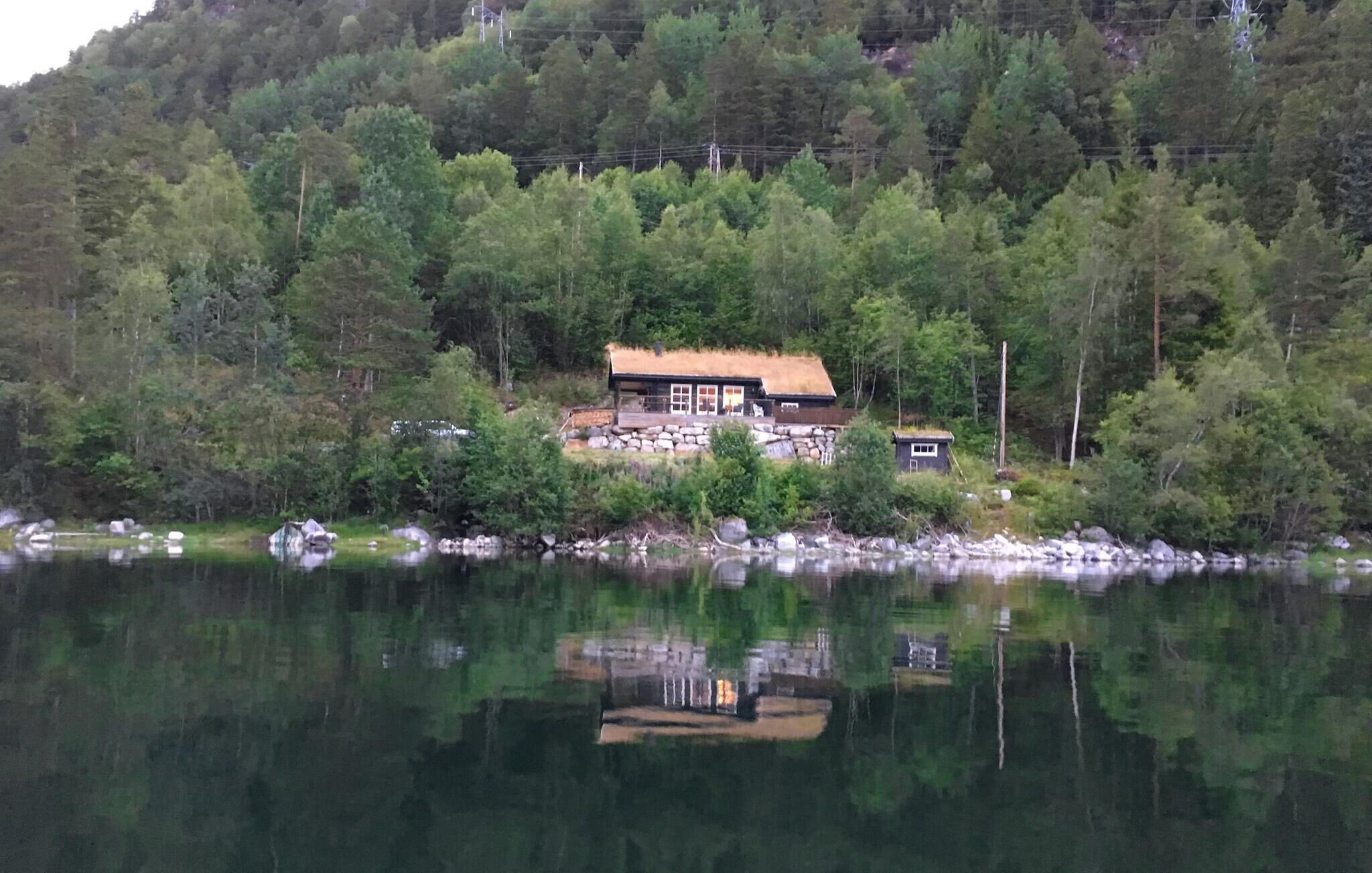 A cabin with a thatched roof, surrounded by dense forest and a calm lake.