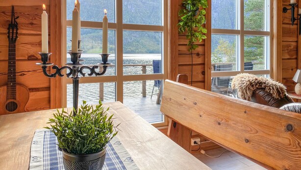 A wooden cabin with large windows overlooking a lake, a table with a potted plant, a bench, and a guitar. - Stunning home in Todalen (Todalen)