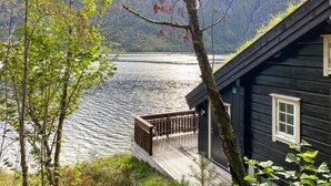 A cabin with a wooden deck overlooking a calm lake, surrounded by trees and mountains. - Stunning home in Todalen (Todalen)