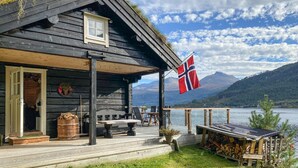 A wooden cabin with a deck, a flag, and a view of mountains and a lake. - Stunning home in Todalen (Todalen)