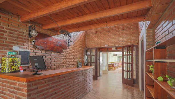 A reception area with a brick wall, wooden ceiling, and a reception desk with a computer monitor. - Posada d'lua (Villa Carlos Paz)