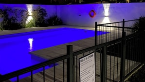 A nighttime swimming pool with blue lighting, a safety sign, and a fence. - Posada d'lua (Villa Carlos Paz)