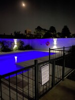 Una piscina iluminada con luces azules, un cartel de seguridad y una valla.