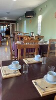 Un comedor con mesas dispuestas para dos, cada una con una taza, platillo y cubiertos.