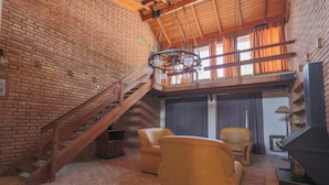 A spacious living area with a brick wall, a wooden staircase, leather chairs, and a fireplace. - Posada d'lua (Villa Carlos Paz)