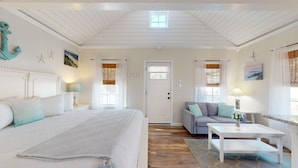 A well-lit room with a large bed, a sofa, a coffee table, and a door with a window. - Coastal Estate – Private Cottage with King Bed & Pool Access (Cape May)