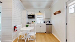 Una cocina compacta con muebles blancos, microondas, cafetera y lavavajillas.