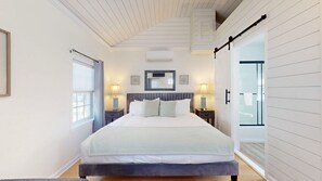 Une chambre à coucher comprenant un lit, des lampes de chevet, un miroir et une porte coulissante donnant sur une salle de bain.