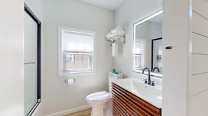 A bathroom with a toilet, sink, mirror, towel rack, and a window.