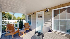 A covered porch with wooden chairs and a table, a door with a mailbox, and a view of the surrounding area.