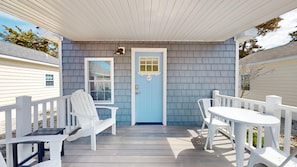 A covered porch with a blue door, white railings, and outdoor furniture.