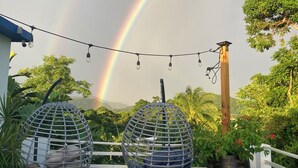 A rooftop terrace with two hanging egg chairs, a string of lights, and a view of a rainbow. - Tropical Retreat with Spectacular Rainforest & Ocean Views. Now with Jacuzzi! (Luquillo)