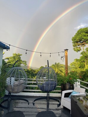 Terraço no telhado com duas cadeiras suspensas em forma de ovo, luzes penduradas e vista de um arco-íris.