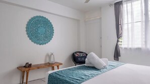 A hotel room with a bed, a small wooden table, a decorative wall hanging, and a window with curtains. - Tropical Retreat with Spectacular Rainforest & Ocean Views. Now with Jacuzzi! (Luquillo)
