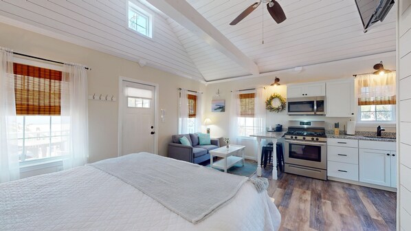 A bedroom with a bed, a small sitting area with a table and chairs, a kitchenette with a stove and microwave, and a door with a coat rack. - Coastal Estate – Private Cottage with King Bed & Pool Access (Cape May)