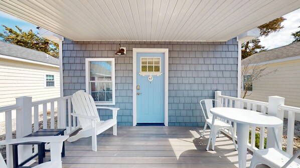 A covered porch with a blue door, white railings, and outdoor furniture.